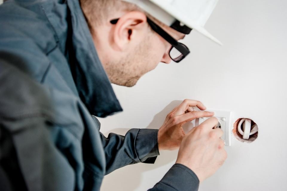 Electrician in a hard hat and safety glasses fitting a wall outlet