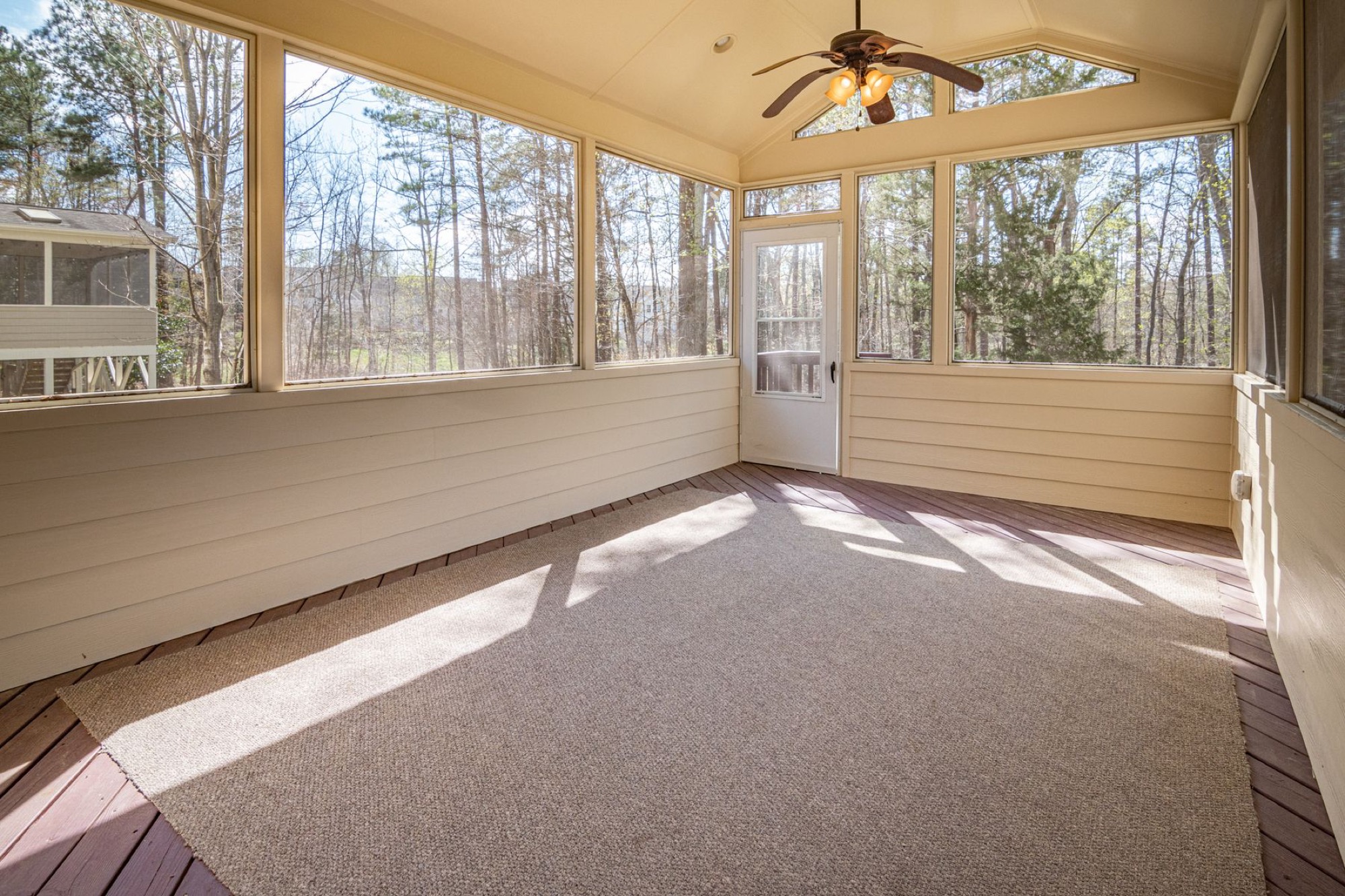Sunlight streams through large windows onto carpeted floor while cooling a sunroom with a ceiling fan